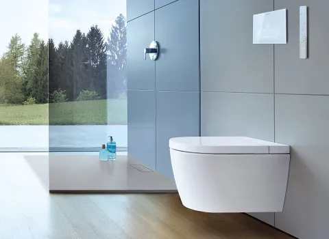 Modernes Badezimmer mit wandmontiertem Dusch-WC, großen Glasfenstern und Blick ins Grüne.